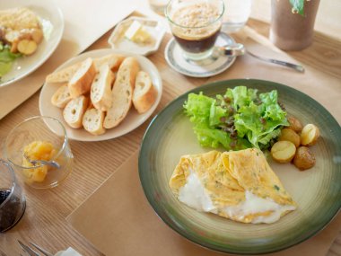 Omlet, kahve, kavrulmuş patates ve beyaz plaka ve gevrek Fransız dilim ekmek, organik salata ile lezzetli Breakfast Jam tahta masada sabah