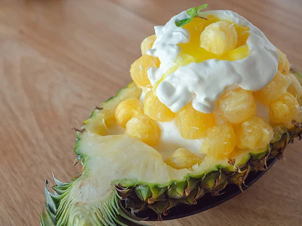 Ice Cream Snow Flake. Sweet Dessert Korean Style call Bingsu with Pineapple Flavor Ice Ball in A Bowl Made by A Half of Fresh Pineapple on Wooden Table Cafe Background
