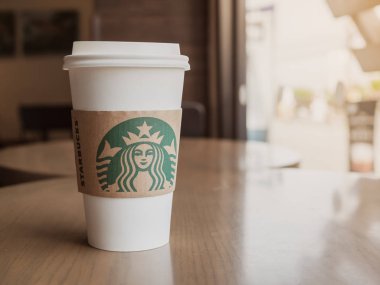 Samut Songkhram, Tayland - 21 Haziran 2018: Beyaz plastik sıcak kahve götürün ahşap masa üzerinde kahve fincanı Starbucks kafede cam pencere yanında.