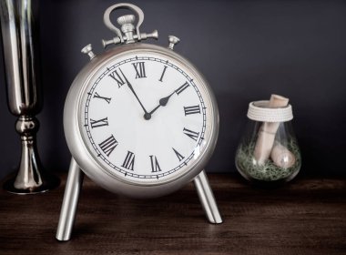 Yakın çekim Paslanmaz Klasik Vintage Romen Rakamlari saat, cam ve vazo. Natürmort koyu arka plan üzerinde ahşap dolap üzerinde.