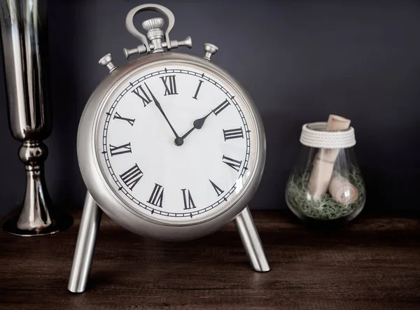 Yakın çekim Paslanmaz Klasik Vintage Romen Rakamlari saat, cam ve vazo. Natürmort koyu arka plan üzerinde ahşap dolap üzerinde.