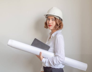 Güzel Asyalı kadın mühendislik kıvırcık kısa saç beyaz kask ve blueprint ve defter tutan beyaz duvar arka plan üzerinde beyaz gömlek giyiyor. Çalışan kadın kavramı.