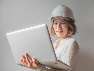 Beyaz kask ve gümüş laptop ile çalışma ve gülümseyen beyaz gömlek giymiş güzel Asyalı kadın mühendis kıvırcık kısa saçlı. Çalışan kadın kavramı.