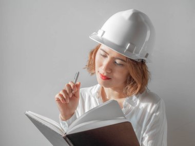 Beyaz kask ve defter ve düşünme fikir ile gümüş kalem tutan beyaz gömlek giymiş güzel Asyalı kadın mühendis kıvırcık kısa saçlı. Çalışan kadın kavramı.