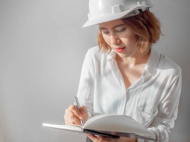 Güzel Asyalı kadın kıvırcık kısa saç beyaz kask ve beyaz gömlek yazılı defter gümüş kalem tarafından giyen mühendislik. Çalışan kadın kavramı.