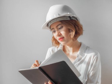 Güzel Asyalı kadın kıvırcık kısa saç beyaz kask ve beyaz gömlek yazılı defter gümüş kalem tarafından giyen mühendislik. Çalışan kadın kavramı.