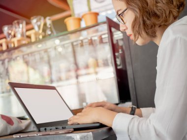 Güzel Asyalı kadın gözlük ve beyaz gömlek giymiş siyah dizüstü bilgisayar ve cep telefonu kafede ahşap masa üzerinde yazarak çalışma, konsantre. Çalışan kadın kavramı.