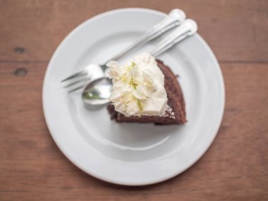 Tepesi ve kırbaçlanan krem beyaz seramik plaka üstüne sillver kaşık ve ahşap masa arka plan üstten görünüm üzerinde çatal ile güzel vintage çiçekler ile vahşi organik çikolatalı bal pasta bir parça.