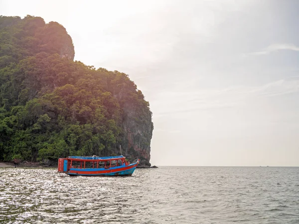 Wooden local travel passenger ferry boat on the sea near the rock mountain on blue sky background with sunlight in Thailand.
