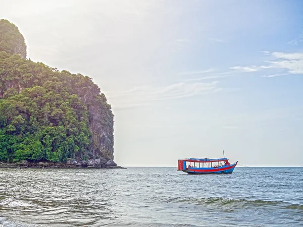 Wooden local travel passenger ferry boat on the sea near the rock mountain on blue sky background with sunlight in Thailand.