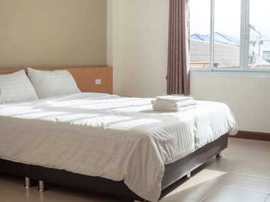 Beyaz temiz yatak odalı otel, yastıklar ve havlu yatak, perdeler ve pencere ışıktan dışarı ile kırsal görünümünde evler.