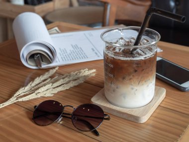 Buzlu kahve kabı Kupası siyah tüp, cep telefonu, güneş gözlüğü ve vintage tarzı cafe ahşap masa kağıda. kahve eşsiz konsepti.