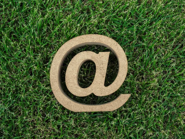 Wooden E-mail address symbol on green grass background, arroba icon on green leaves background with copy space. E-mail marketing online internet, technology and environment concept.