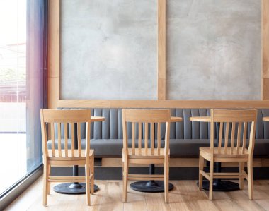 Boş yer beton duvar ve ahşap sandalyeler, ahşap yuvarlak masa ve cam pencere duvarı yakınındaki kafede yerleşik deri kanepe.