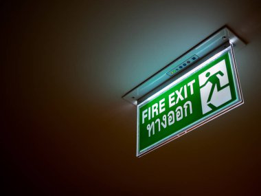 Yangın çıkış işareti. Acil durum Led Aydınlatma işareti tavan kopya alanı ile koyu arka plan üzerine monte. (Tay dili metin de ortalama yangın çıkışı)