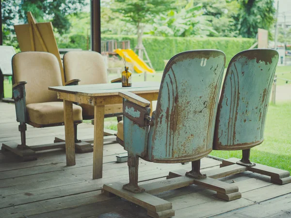 Vintage theatre seats with wooden table on wooden floor on green park background in retro style cafe. Unique mix and match furniture style concept.