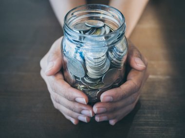 Cam kavanoz ahşap masa arka plan üzerinde elinde para çıktı. Para ve bağış kavramı kaydetme.