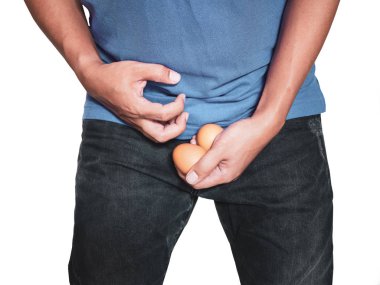 Adam beyaz arka plan üzerinde izole ağrı eylem ile pantolon orta kasık üzerinde yumurta tutan eller.