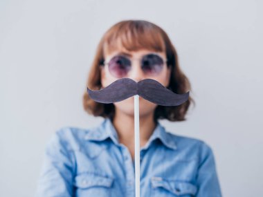 Güzel Asyalı kadın kısa saç beyaz arka plan üzerinde izole sahte bıyıklı kot gömlek ve güneş gözlüğü takıyor.