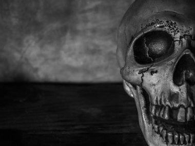 Yakın çekim korku insan kafatası yüz eski ahşap masa ve çimento grunge duvar arka plan üzerinde siyah beyaz stil üzerinde kopya alanı ile.