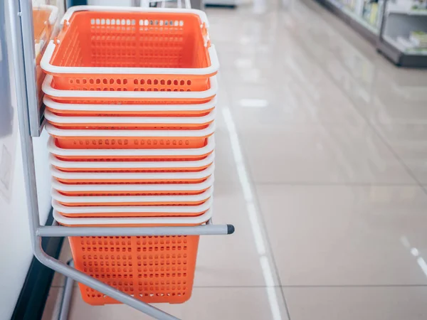 Row of orange shopping basket in storage shelf on the clean floor with copy space. Shopping basket service for customer using in mini mart.