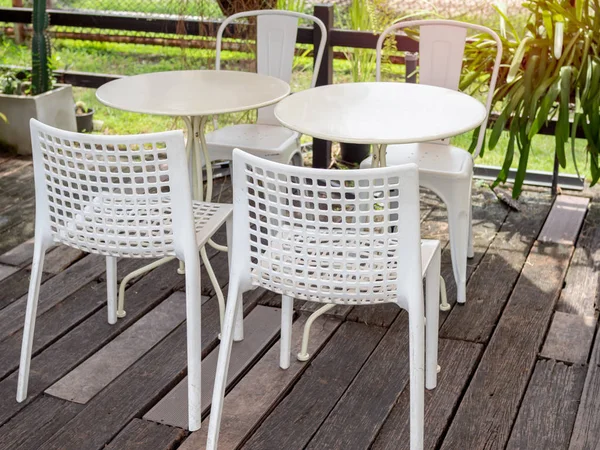 White modern mixed and match round tables and chairs on old wooden floor near the garden in retro cafe.