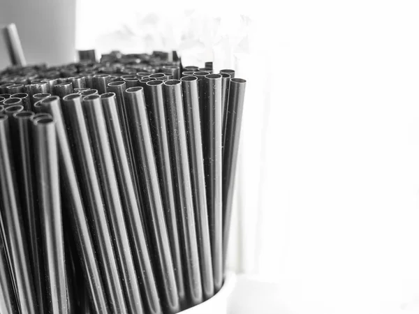 Dirty black coffee straws in white ceramic mug on white background with copy space.