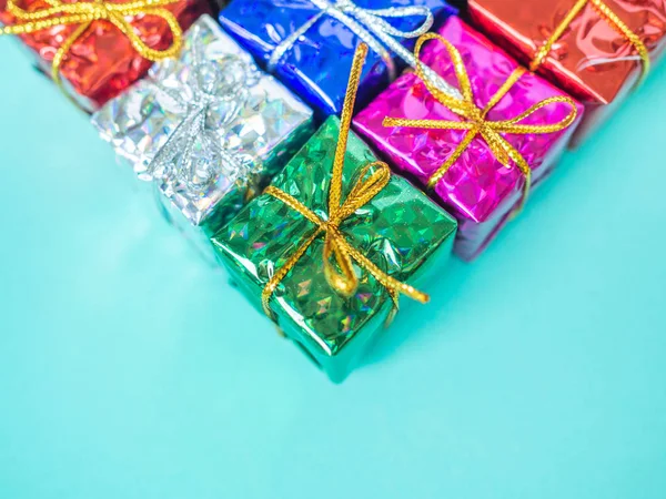 Small colorful gift boxes on light marine blue background with copy space. Top view of many gifts wrapped colorful shiny paper.