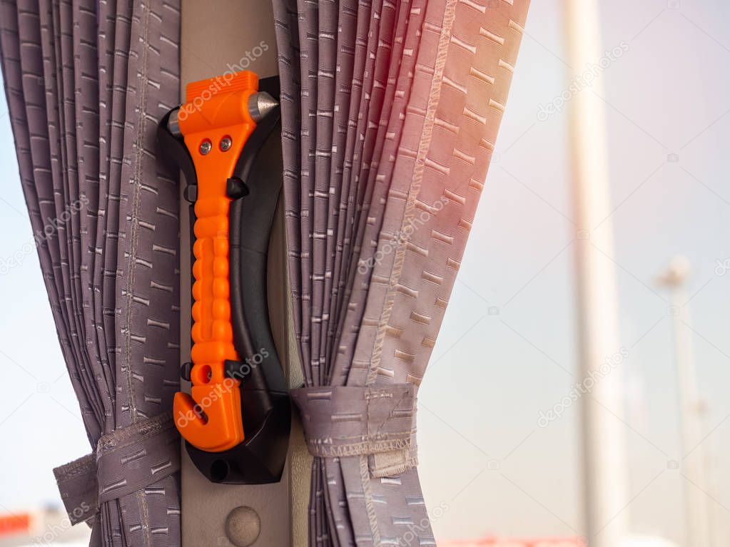 Orange safety hammer mounting near the window glass and curtain on the bus, use in case accident.