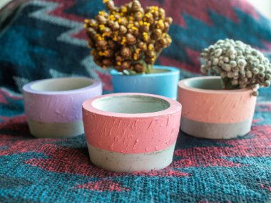 Renkli yuvarlak geometrik beton yetiştiricilerinin çiçekli kumaş arka plan üzerinde. Modern güzel beton pot, ev ve bahçe dekorasyon konsepti boyalı.