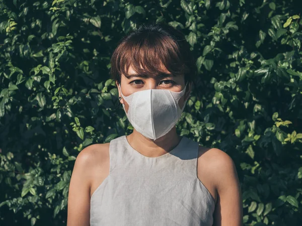 Beautiful asian woman wearing white protective N95 dust mask on green leaves background. Protection against pollution concept.