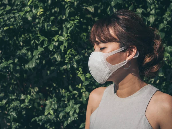 美しいアジアの女性は 彼女の目とコピー スペースと緑の葉の背景に白い保護 N95 防塵マスク身に着けているを閉じます 汚染概念に対する保護 — ストック写真