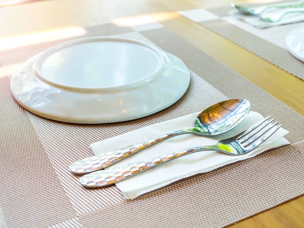 White plate with spoon and fork on the plate mat on wooden table — Stock Photo, Image