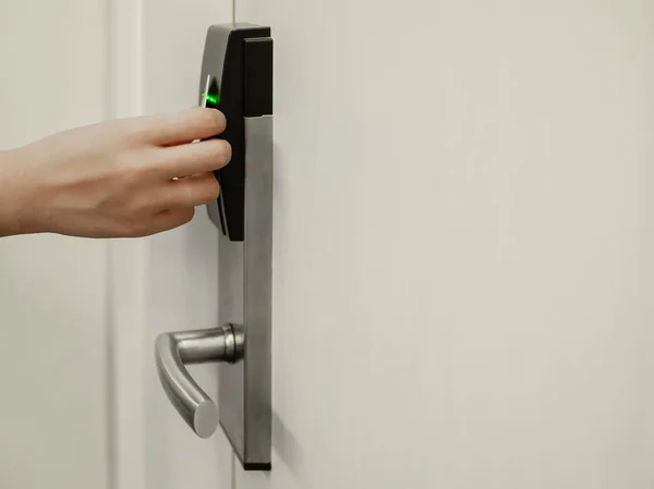 Hand holding key card in front of electronic lock to open white