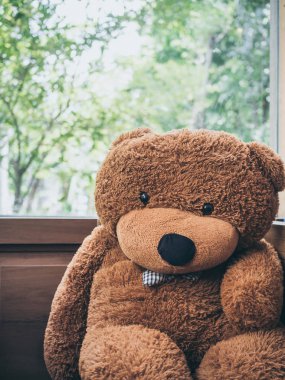 Büyük sevimli oyuncak ayı pencere cam yanında oturan