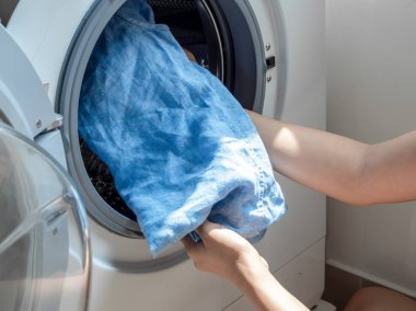 Çamaşır makinesine kirli mavi keten gömlek koyan kadın eli.