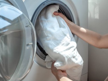 Çamaşır makinesine kirli beyaz keten gömlek koyan kadın eli.
