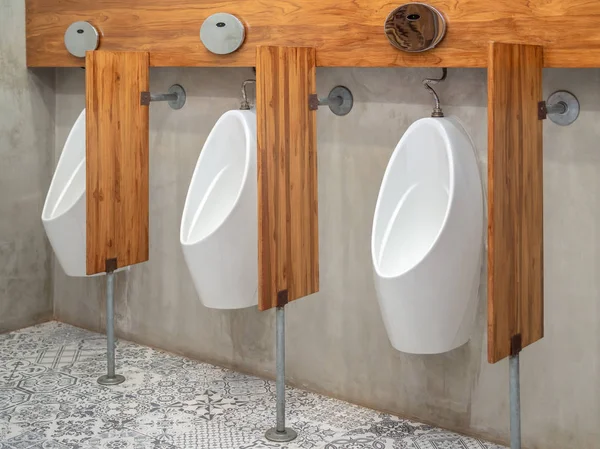 Three modern white automatic urinal for men and wood partitions