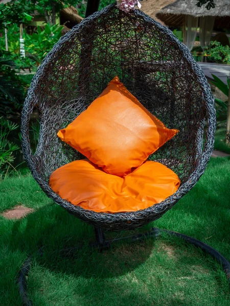 Rattan lounger hanging egg chair with orange pillow. — Stock Photo, Image