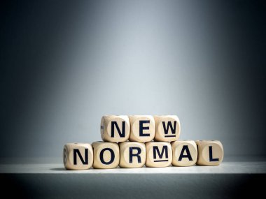 Spot ışıkları New Normal 'da parlıyor, kelimeler koyu arkaplanda tahta alfabe küpünde. Covid-19 salgınından sonra yeni normal.