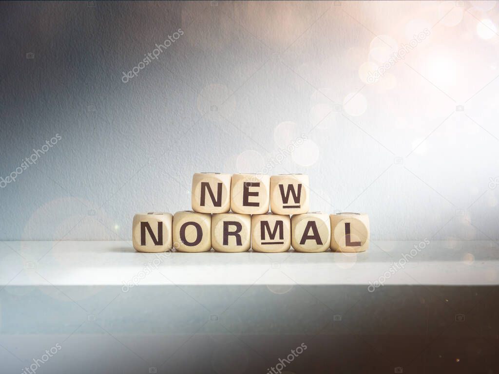 Beautiful bokeh from sunlight shines on New Normal, words on wooden alphabet cube on dark background. New normal after covid-19 pandemic concept.