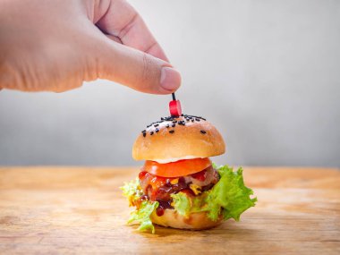 Ev yapımı hamburger hazır. Lezzetli küçük ev yapımı sulu hamburgerin üzerine kırmızı kokteyl penası koyun. Biftek, peynir, taze dilimlenmiş domates, yeşil marul ve ahşap kesme tahtasındaki karamelize soğan..