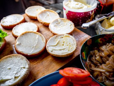 Lezzetli ev yapımı hamburgerler yapma süreci. Tereyağlı çörekler, karamelli soğanlar, ahşap kesme tahtasındaki taze domatesler, ev yapımı hamburgerler yapmaya hazır..
