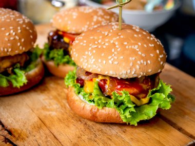 Ev yapımı hamburger hazır. Biftek, peynir, taze yeşil marul ve ahşap kesim tahtasının üzerinde karamelize soğanlı ev yapımı sulu burger..