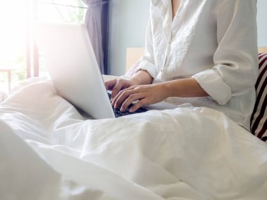 Kadının elleri evin içindeki yatakta dizüstü bilgisayarda yazarken camdan içeri güneş ışığı giriyor. Evde rahatlıkla çalışmak..