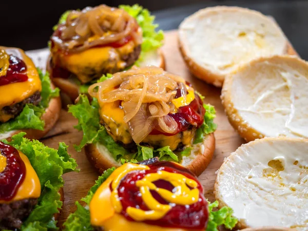 Tasty homemade juicy burger. Caramelized onion on mustard and ketchup on beef, cheese and fresh green lettuce on wood cutting board, process of making delicious homemade burgers.