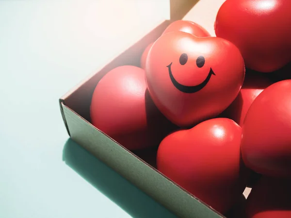 Red hearts with happy and smiling face on many red ball foam with heart shape in brown paper craft box on white background. Love, care, share, donation and Valentine Day Concept.