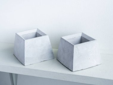Beton çömlek. Beyaz arka planda beyaz ahşap rafta iki boş modern geometrik çimento ekicisi.