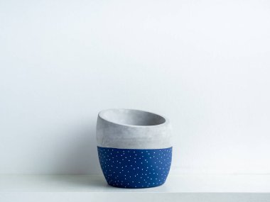Beyaz raftaki boş modern geometrik beton ekiciler beyaz duvar zemininde kopya alanı ile izole edilmiş. Güzel mavi renk ve beyaz nokta deseni boyalı çimento tenceresi.