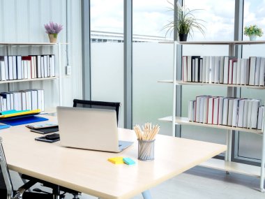 Modern ofis içi kocaman pencereli. Çağdaş işyerinin köşesinde kitap rafı olan ahşap masa. Yeni çalışanın iş görüşmesinde büyük masada dizüstü bilgisayarlı iki boş sandalye..